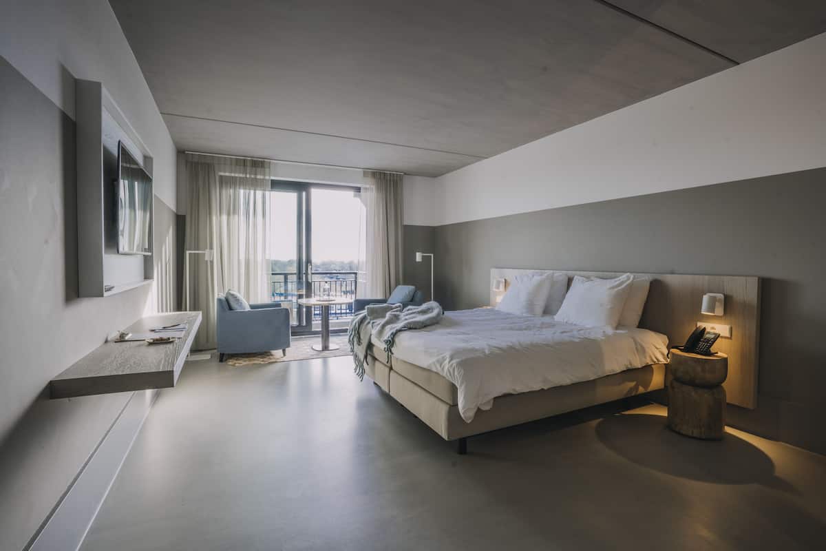 Una habitación de hotel moderna con una cama grande, un escritorio, una silla y un balcón con vistas.