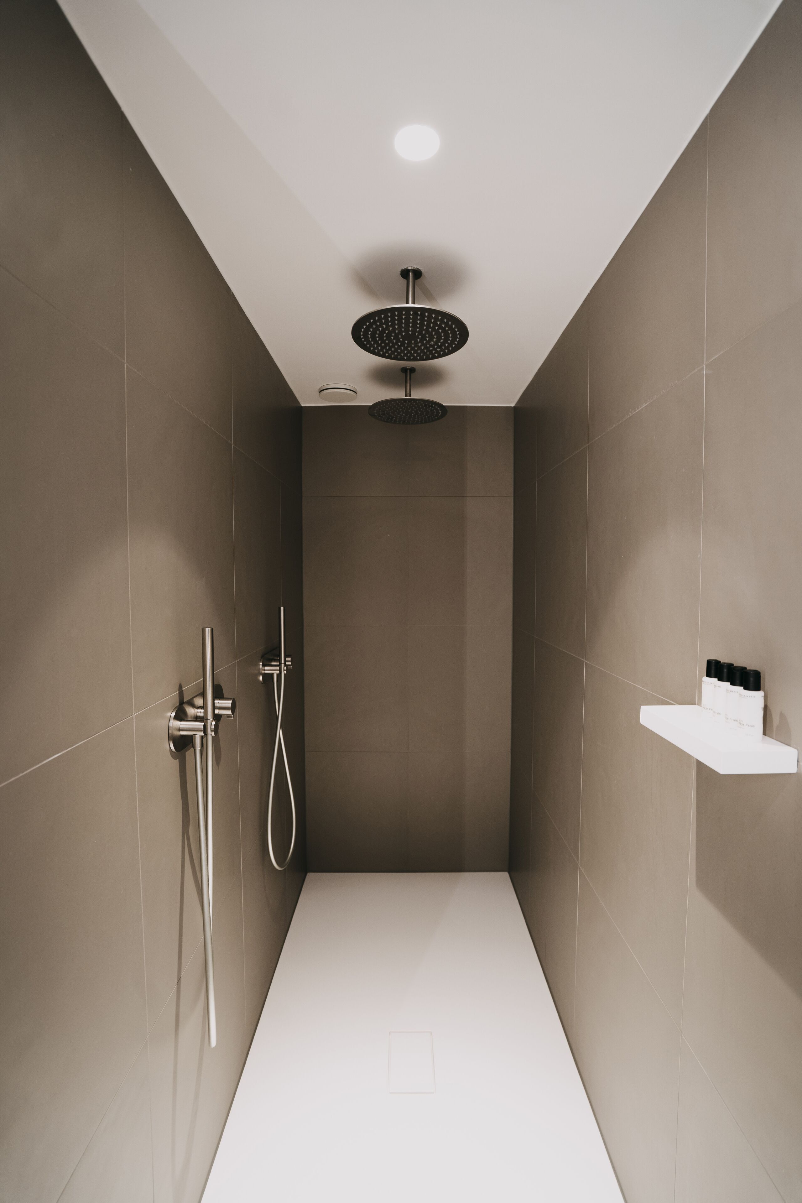 Une douche moderne dotée d’un pommeau de douche rond, d’un pommeau de douche à main et d’une étagère murale pour les articles de toilette.