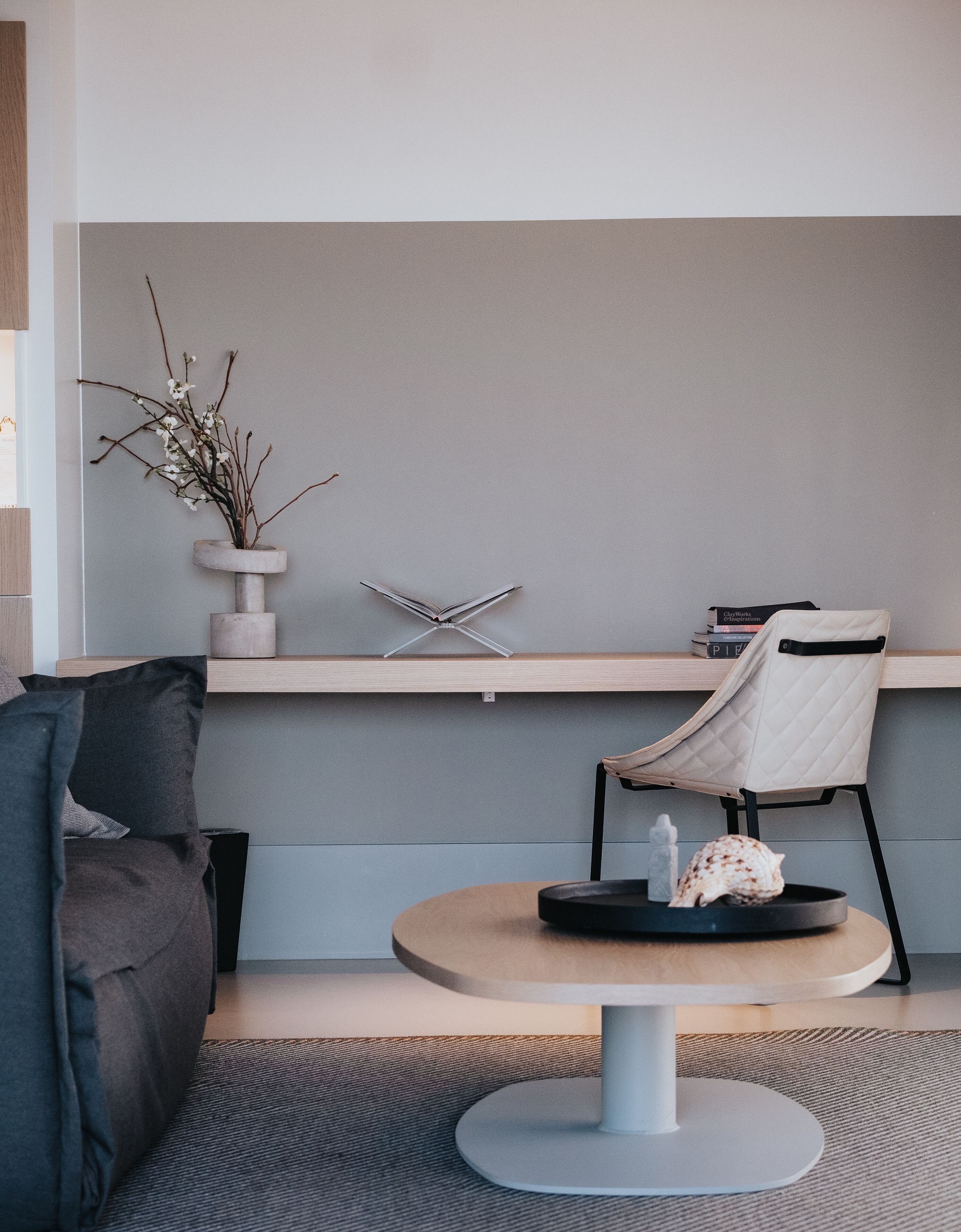Una sala moderna con una mesa redonda, un sillón cómodo, una mesita auxiliar con un jarrón de flores y una estantería con libros.