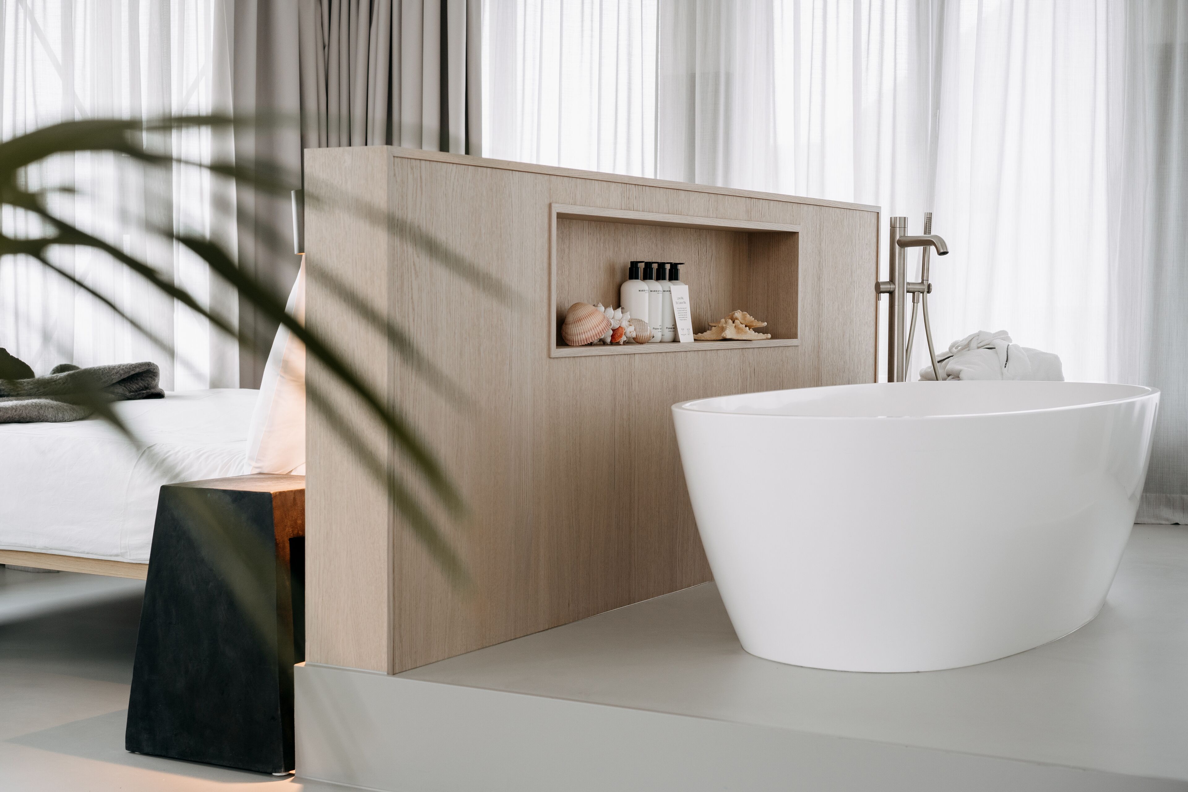 A modern bathroom with a freestanding bathtub, wooden vanity, and a shelf with toiletries.