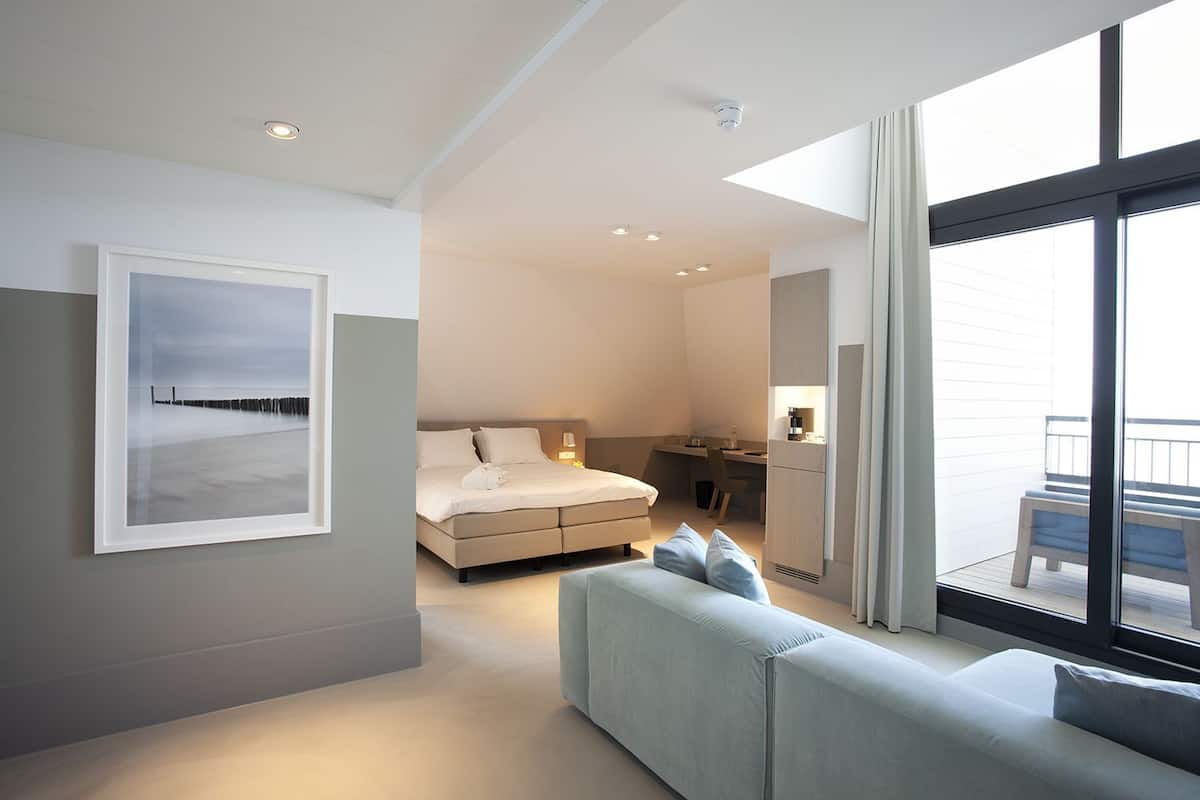 Una habitación de hotel moderna con cama, escritorio, sofá y un amplio ventanal.