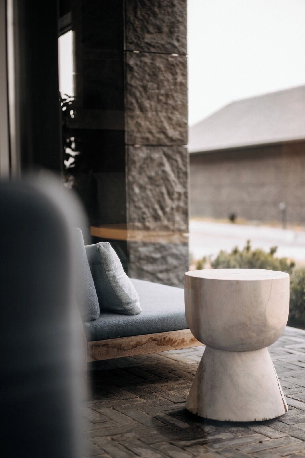 A modern outdoor seating area with a stone pillar, a cushioned bench, and a round table.