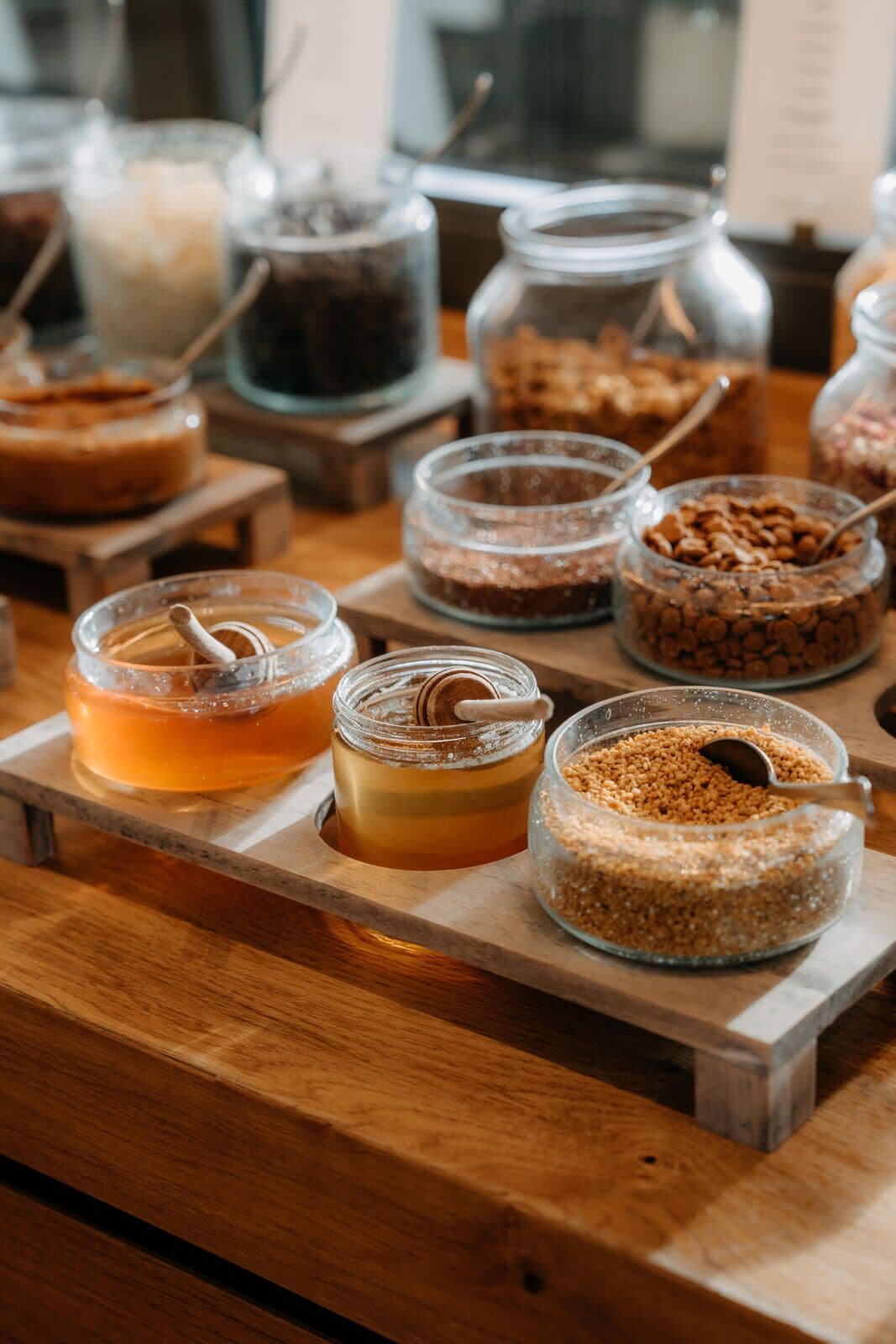 A wooden table with various food items and drinks, including jars of honey, jars of nuts, and a glass of tea.