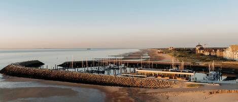 A coastal marina with boats docked, a sandy beach, and a building with a dome structure.