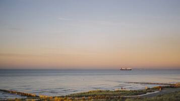 A coastal landscape with a calm sea, a pier, and a ship in the distance.