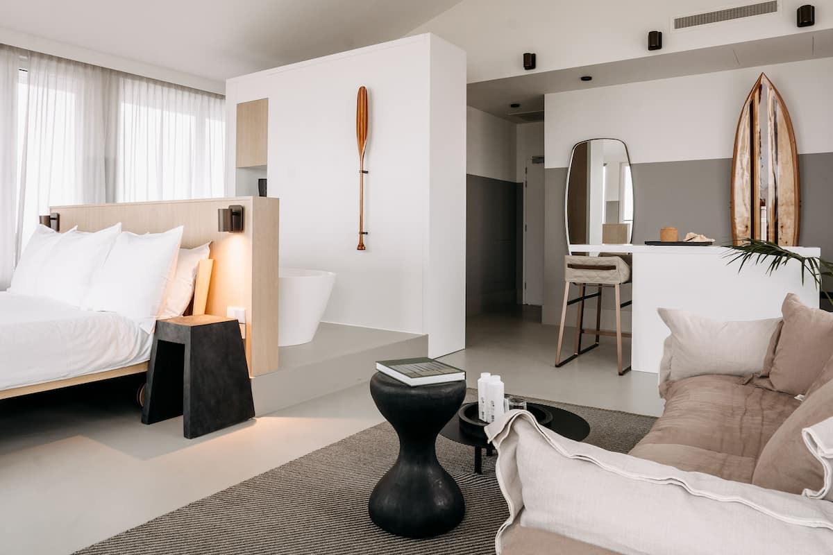 Una habitación de hotel moderna con cama, mesita de noche y un área de descanso con sofá y mesa de centro.