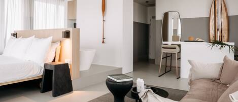 A modern hotel room with a bed, bedside table, and a seating area with a sofa and coffee table.