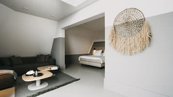 Een moderne loft slaapkamer met een schuine plafond, een groot bed, een zithoek met een bank en salontafel, en een decoratieve droomvanger aan de muur.