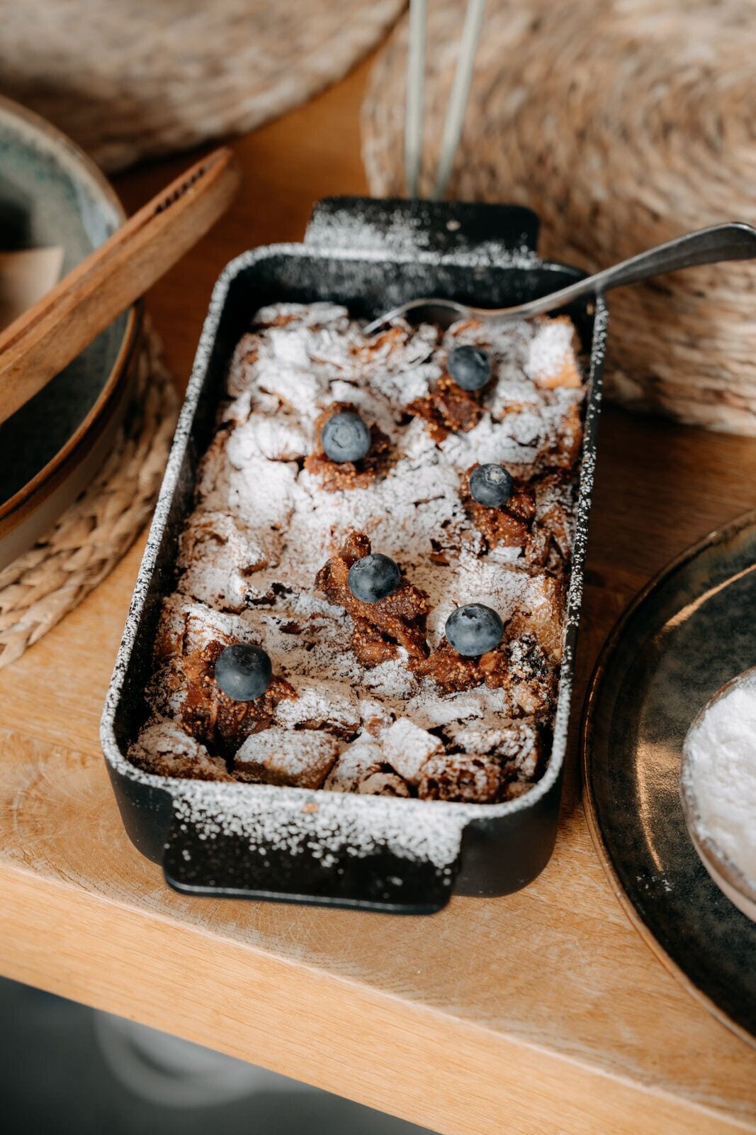 A rectangular baking dish with a dessert, possibly a crumble or cobbler, topped with powdered sugar and blueberries.