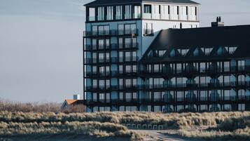 Een modern gebouw met meerdere verdiepingen en een toren, gelegen nabij een strand waar iemand over het zand loopt.