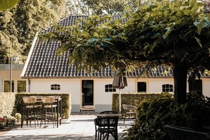 Un edificio con tejado de tejas, una puerta con la leyenda "Brasserie de Hoeve" y terraza con sillas y mesas.