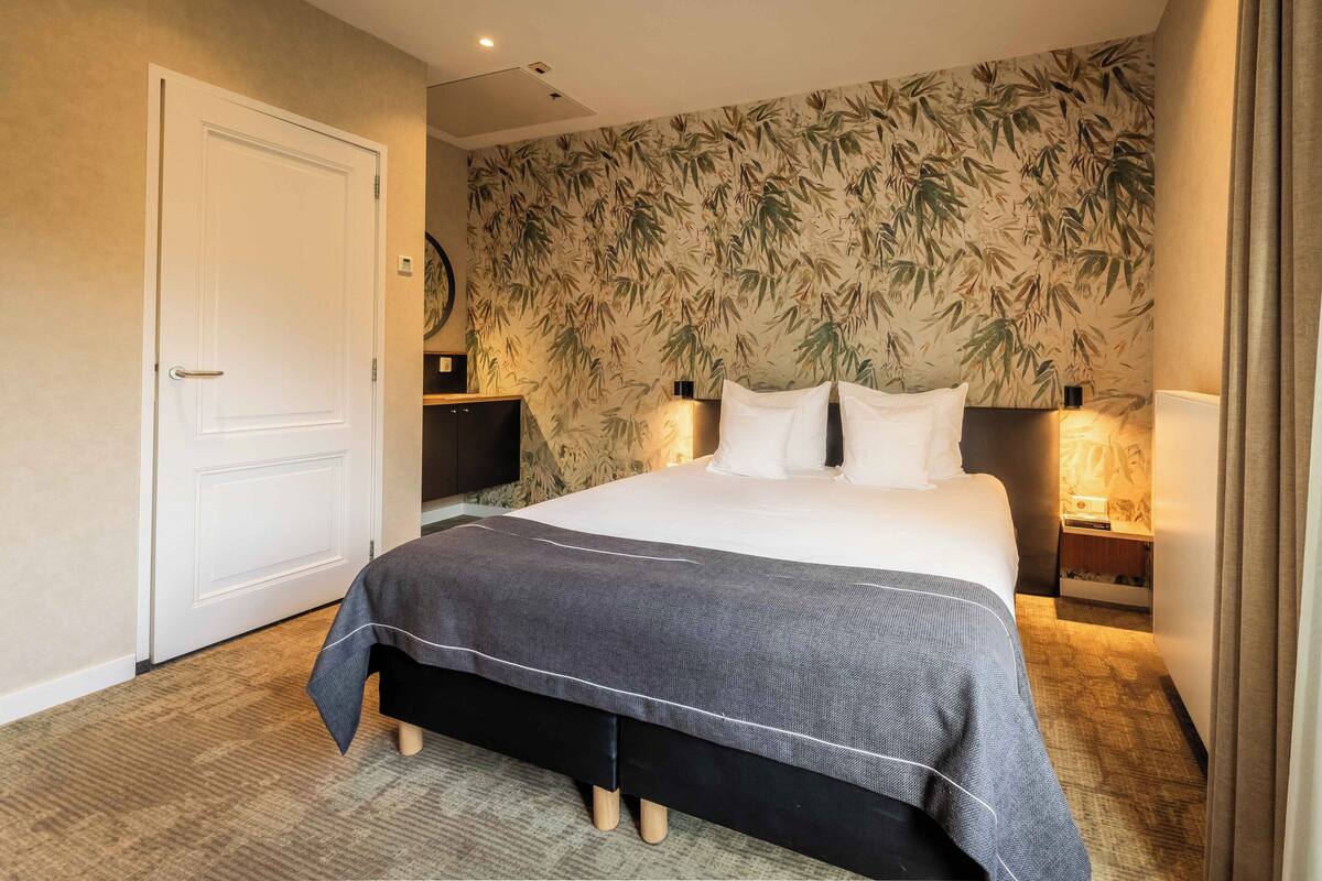 Hotelkamer met een groot bed, twee nachtkastjes, een wand met bamboe bladbehang en een deur.
