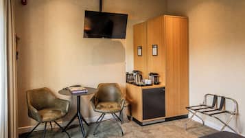 Quarto de hotel compacto com duas poltronas de couro, uma mesa pequena, cozinha compacta e televisão na parede.
