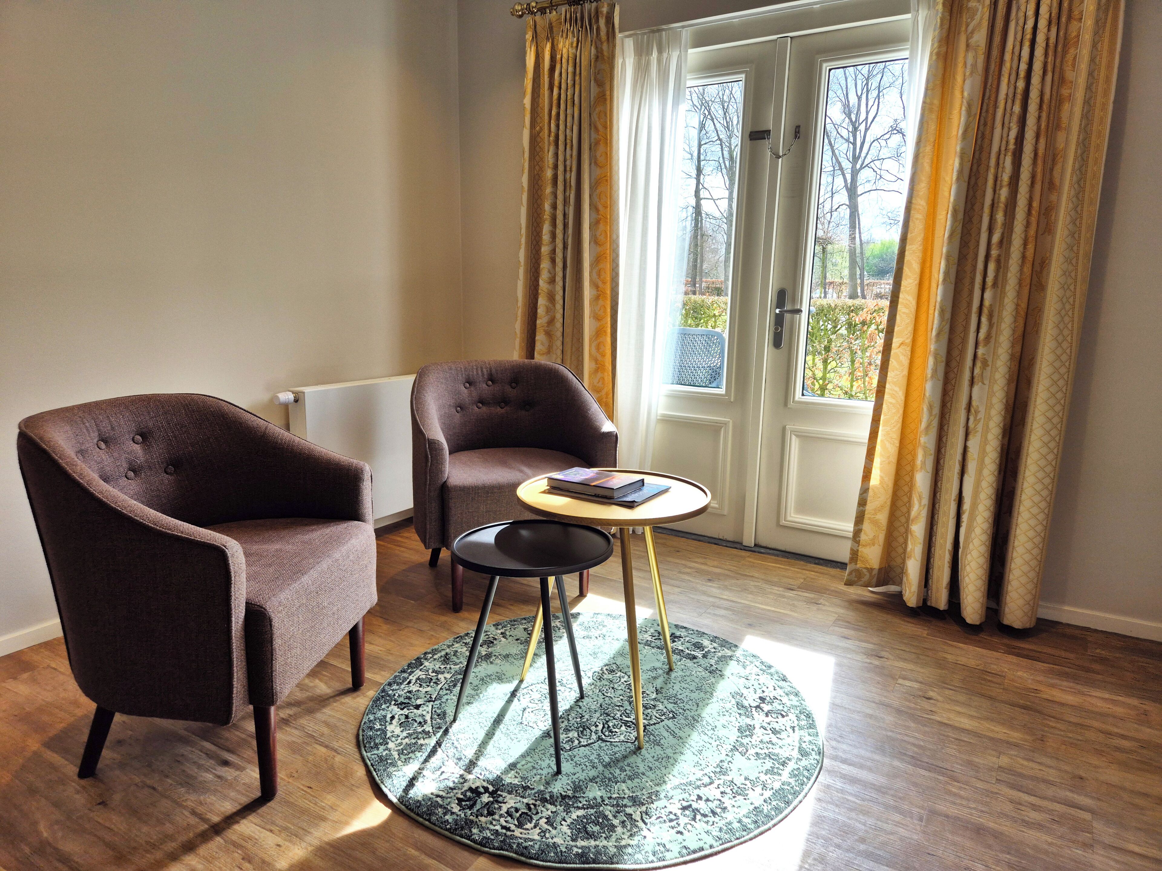 A room with two armchairs, a small round table, and a view through a glass door.