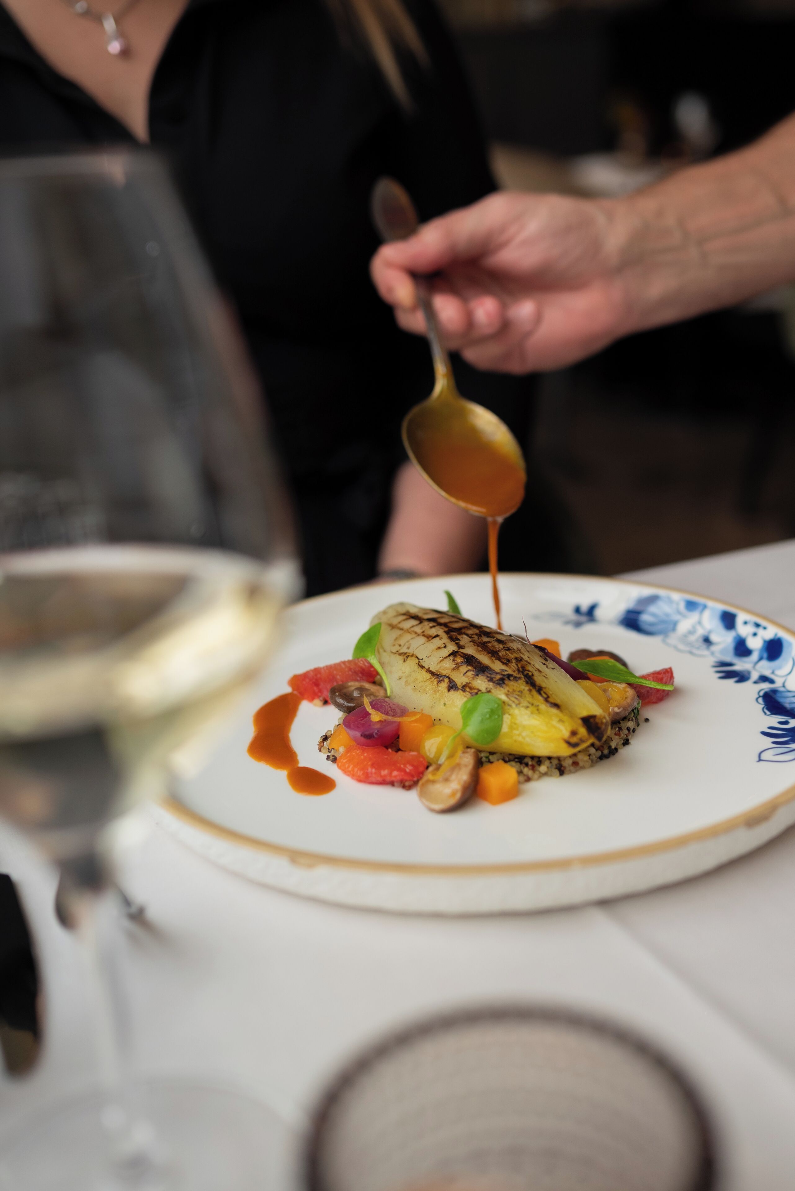 A person pouring sauce over a dish on a plate.