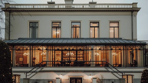 Un edificio amplio y elegante con un patio cubierto, numerosas ventanas y una escalera que conduce a la entrada.