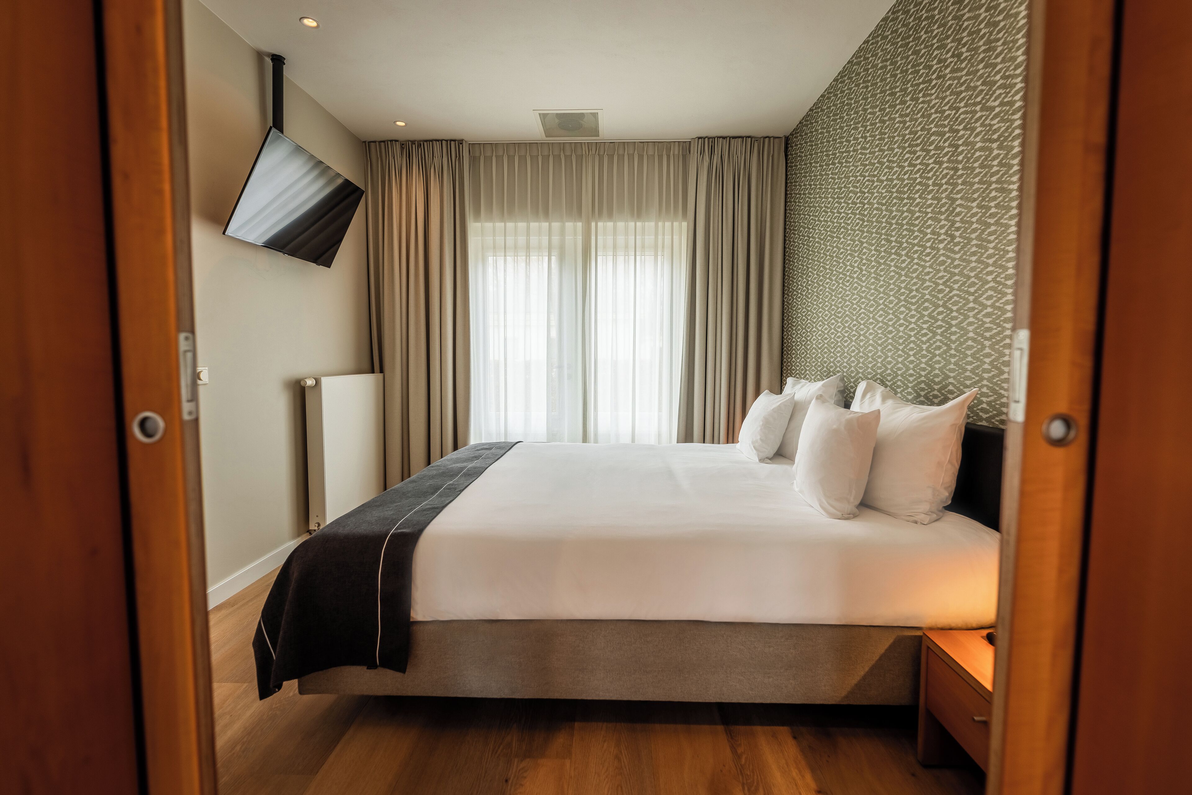 Habitación de hotel con una cama grande, un televisor de pantalla plana en la pared y una ventana con cortinas.