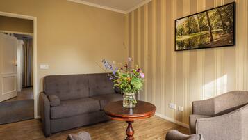 Una sala de estar con un sofá, sillones, una mesa redonda de madera con un jarrón de flores y un cuadro en la pared.