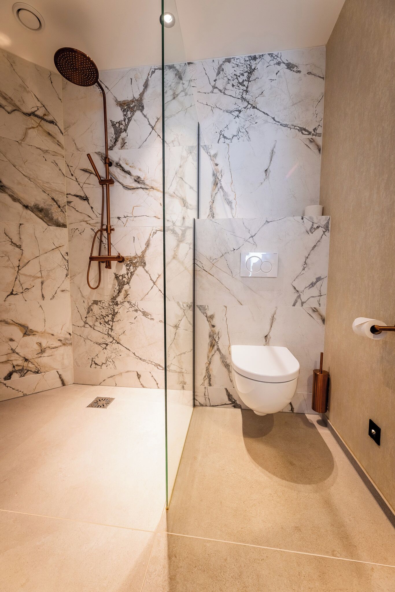 Un baño moderno con cabina de ducha de vidrio, paredes de mármol y un inodoro blanco.