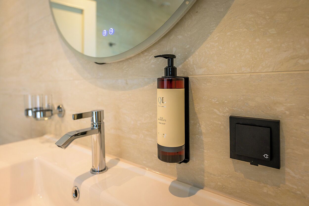 A bathroom with a modern sink, a mirror, and a bottle of lotion mounted on the wall.