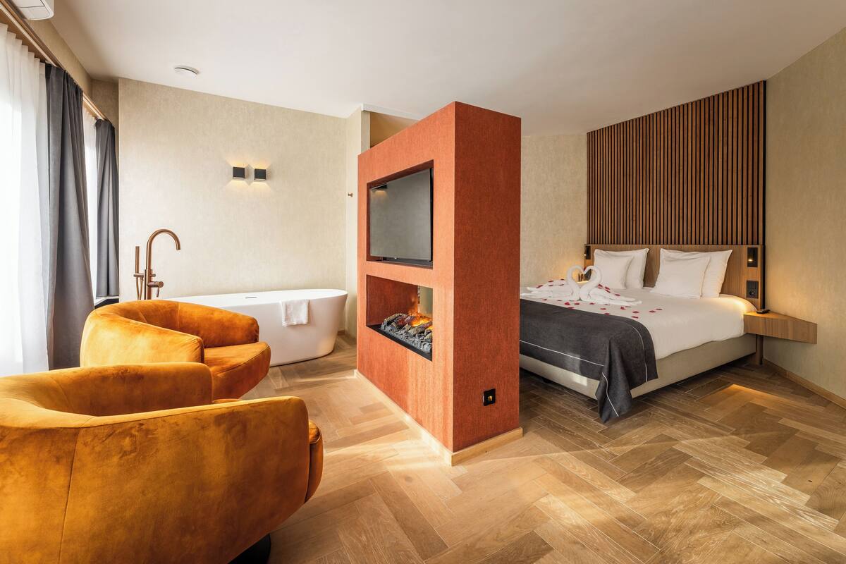 Een moderne hotelkamer met een bank, een bed, een televisie, een open haard en een badkamer.
