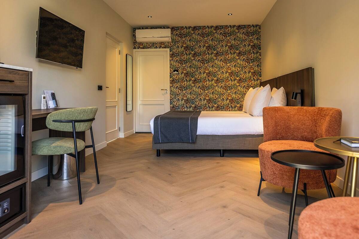 Een hotelkamer met een bed, een bureau met stoel, een klein tafeltje en een aan de muur bevestigde televisie.