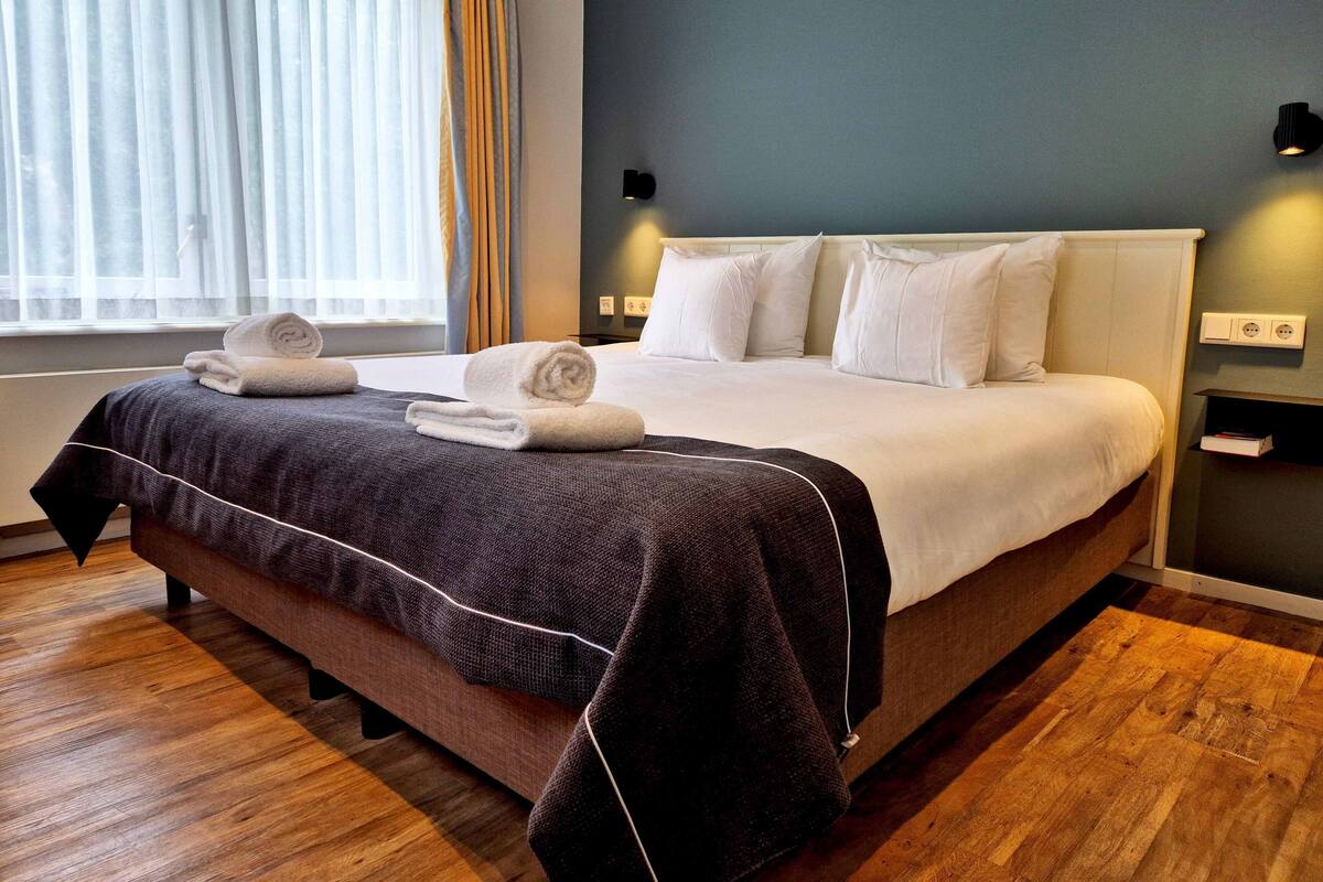 Een hotelkamer met een bed, nachtkastje, lamp en raam met gordijnen.