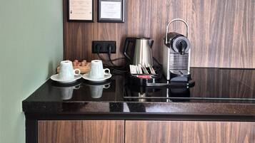 Una encimera de cocina con una cafetera, una taza y un platito. Hay diplomas enmarcados en la pared.