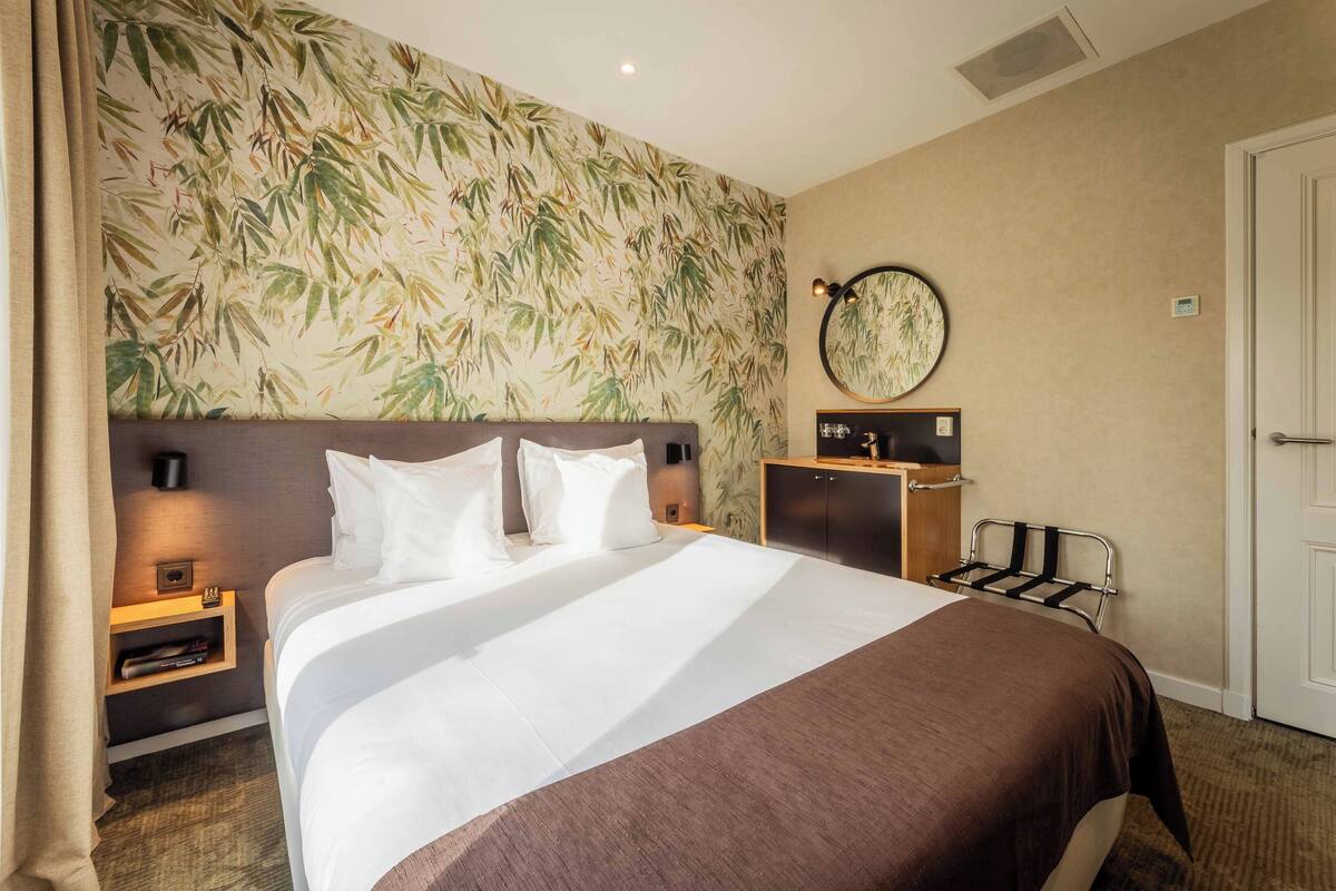 Een hotelkamer met een groot bed, nachtkastje, spiegel en een deur.
