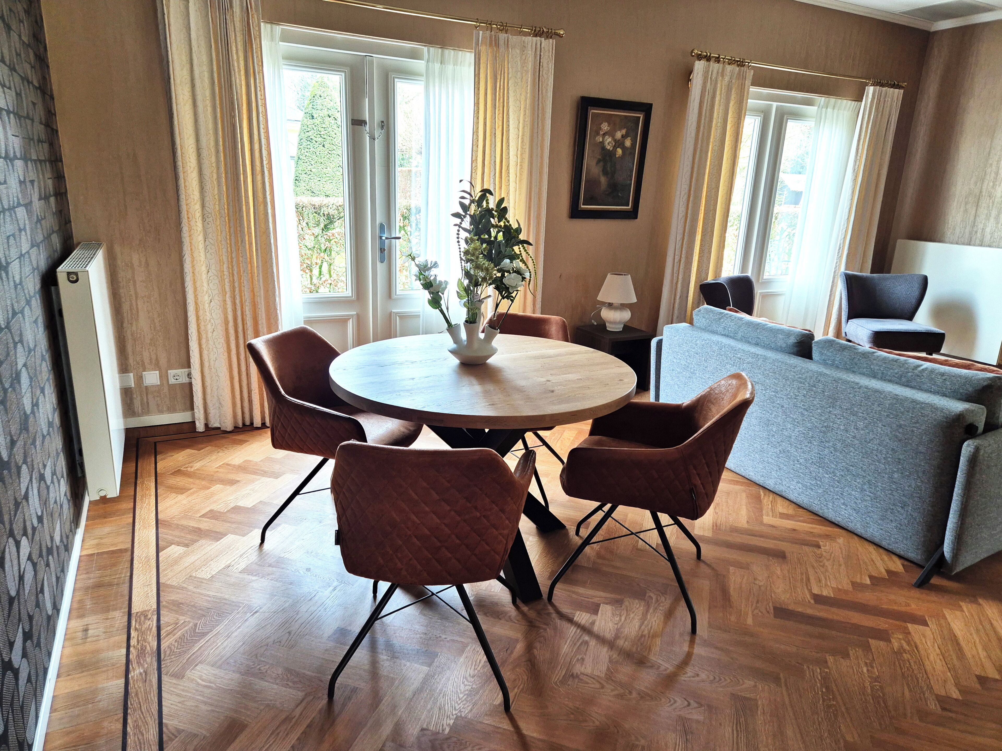 Ein Zimmer mit einem runden Holztisch, vier Stühlen, einem grauen Sofa und einem Blumentopf.