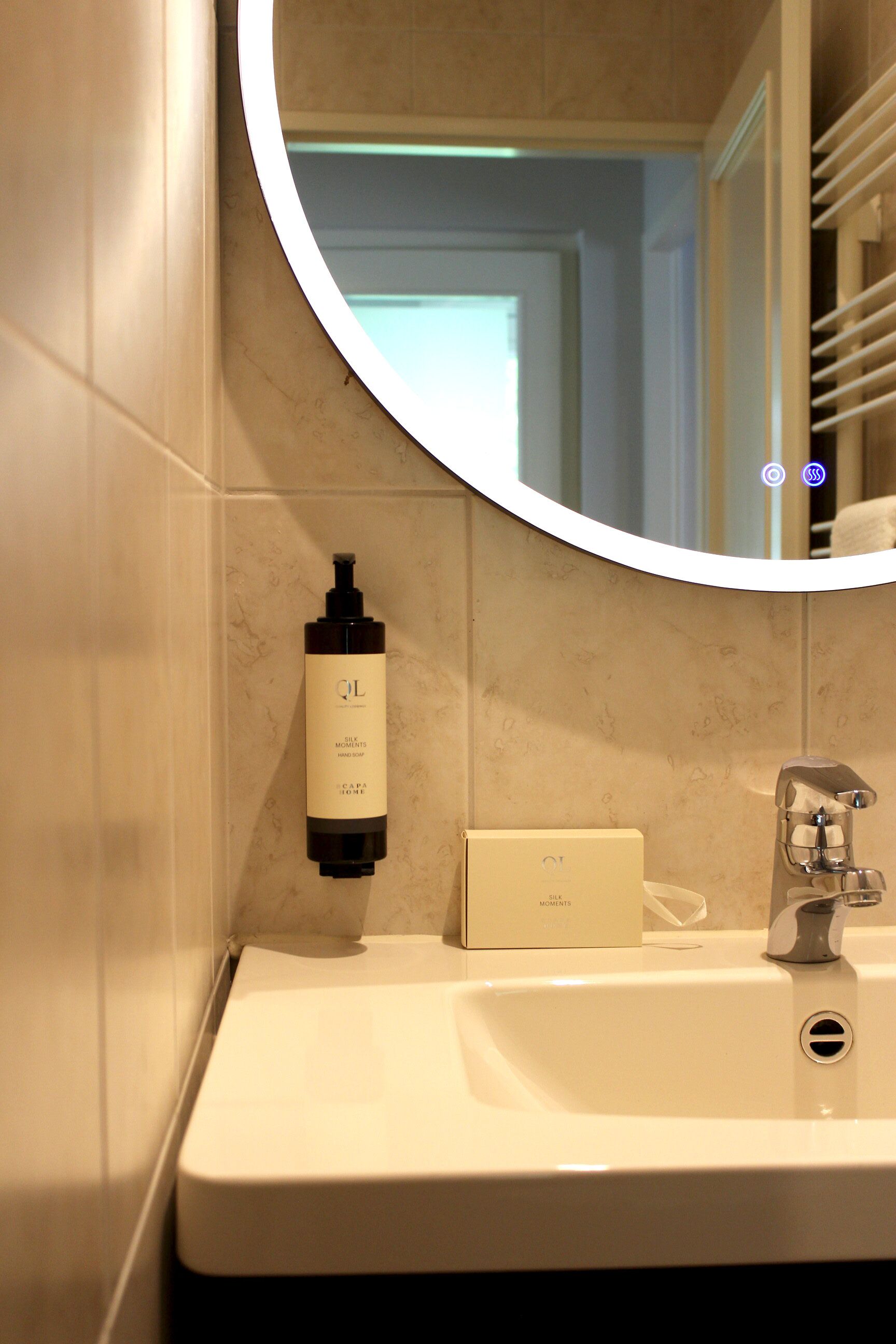 Un baño con un lavabo blanco, un espejo y una botella de loción.