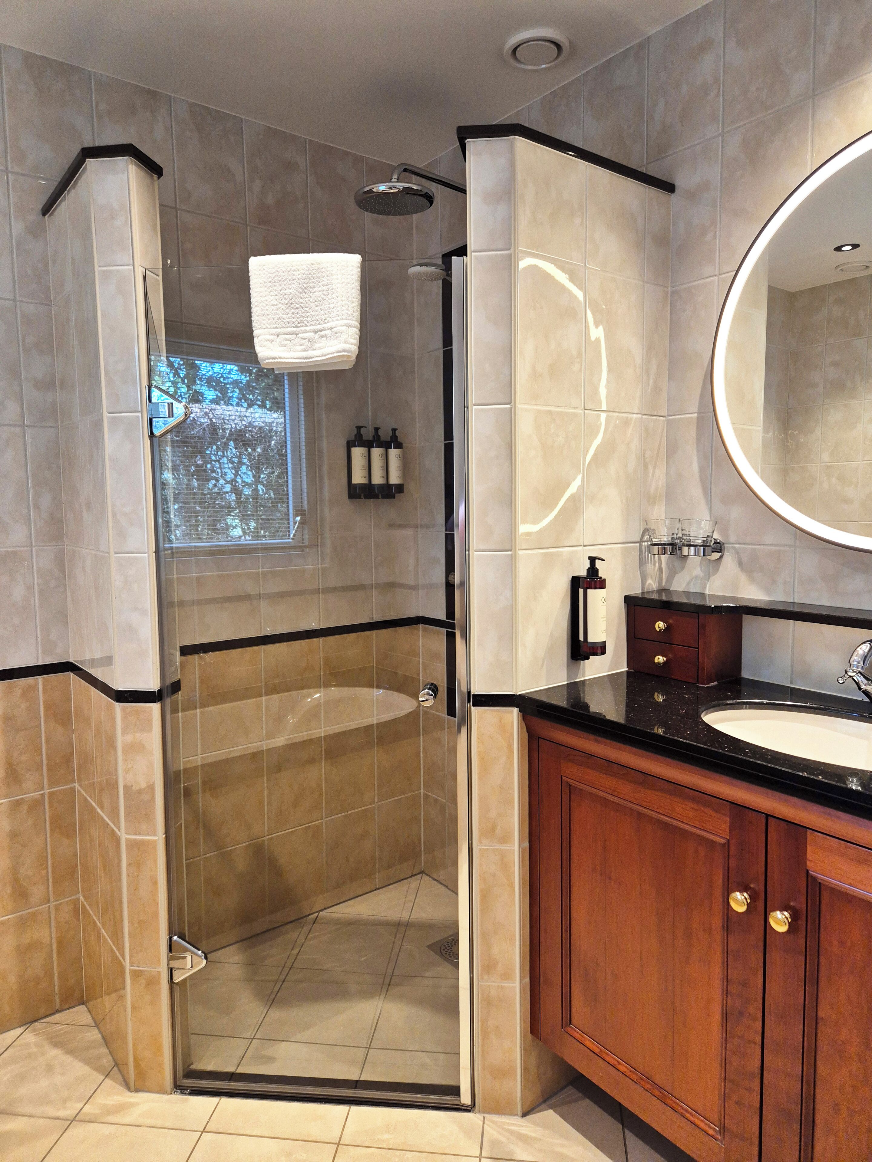 A modern bathroom with a glass-enclosed shower, a vanity with a sink, and a large mirror.