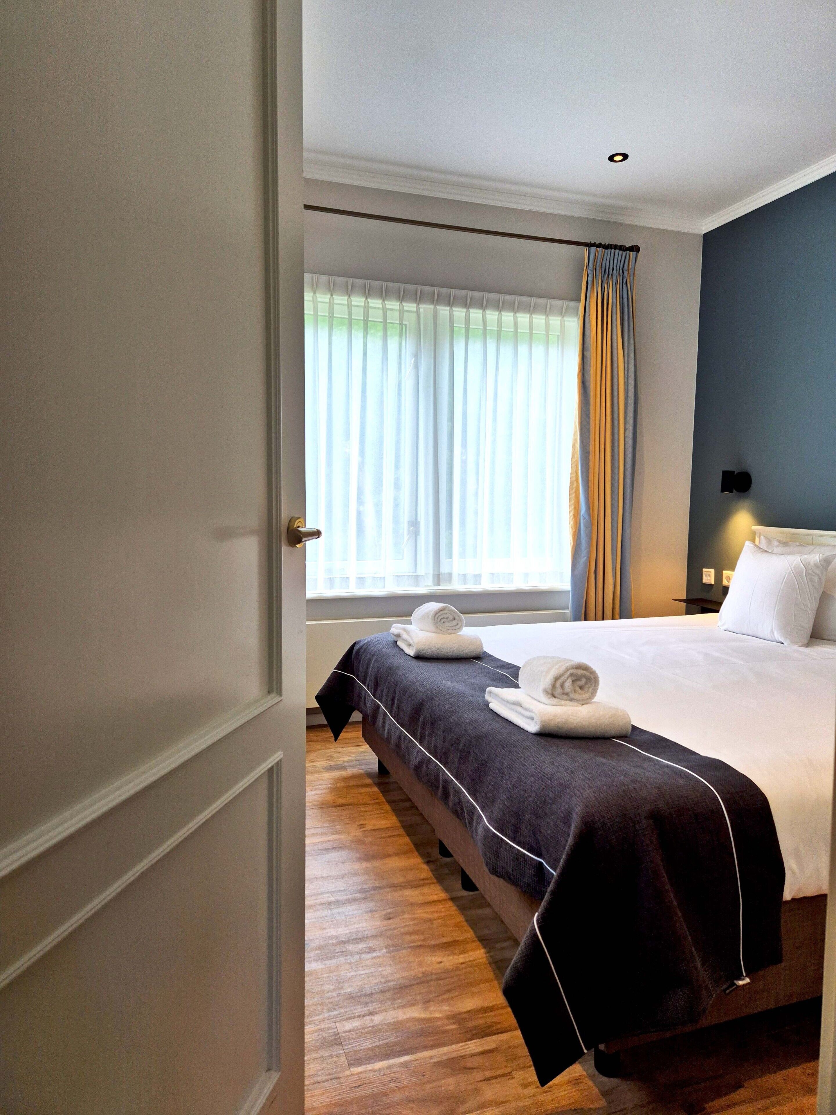 Una habitación de hotel con cama, ventana con cortinas y puerta.
