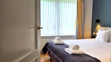 Una habitación de hotel con cama, ventana con cortinas y puerta.