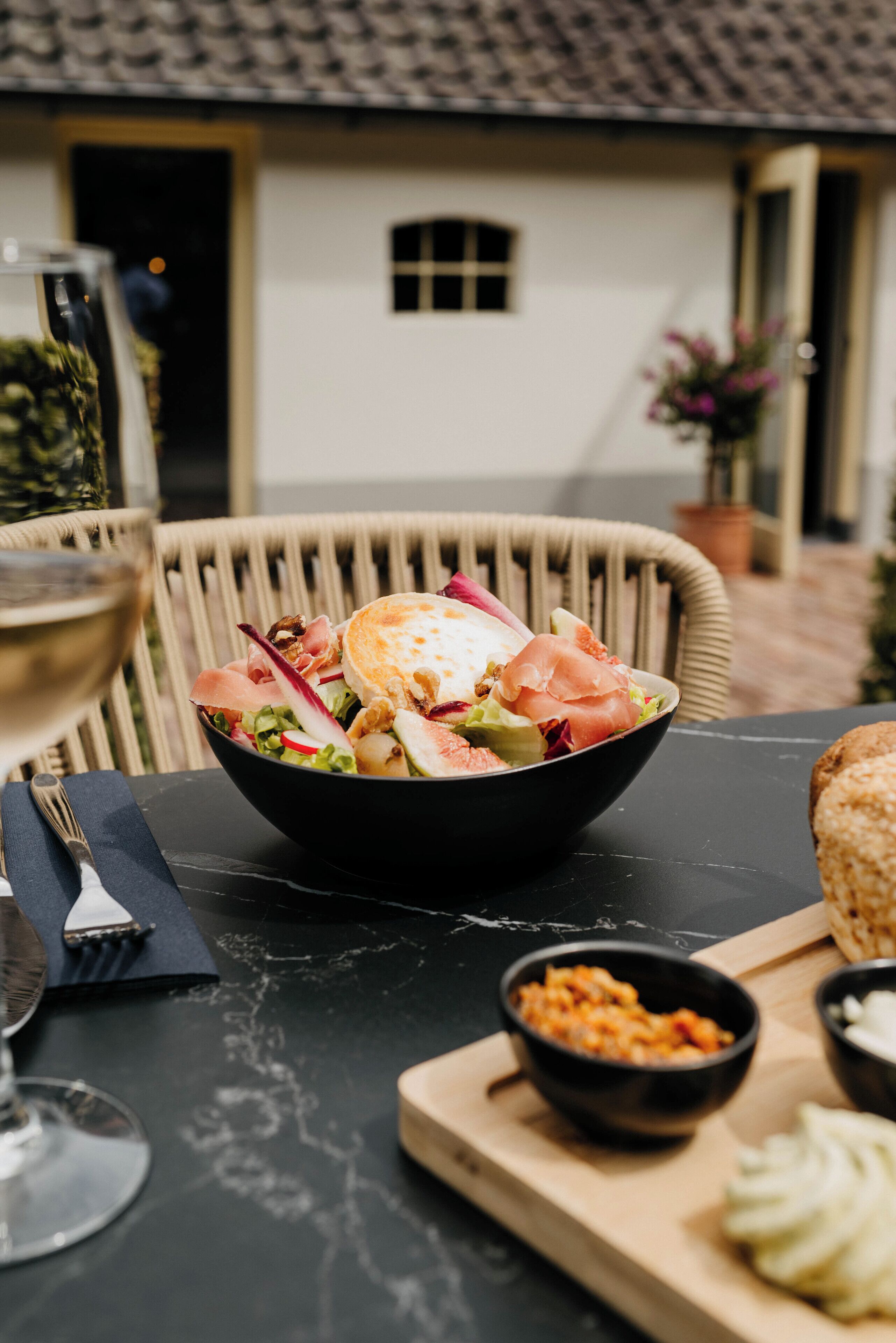 Una mesa de comedor con un bol de ensalada, una copa de vino y un panecillo.