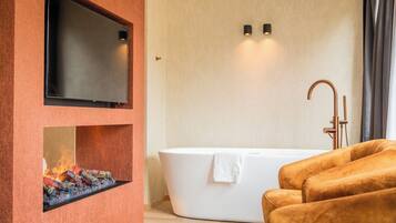 Un baño moderno con chimenea integrada, un televisor de pantalla plana grande, una bañera independiente y un perchero para toallas.