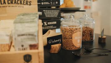 A table with various food items, including boxes labeled 'La Crackers' and 'Gluten Free', and jars of granola.