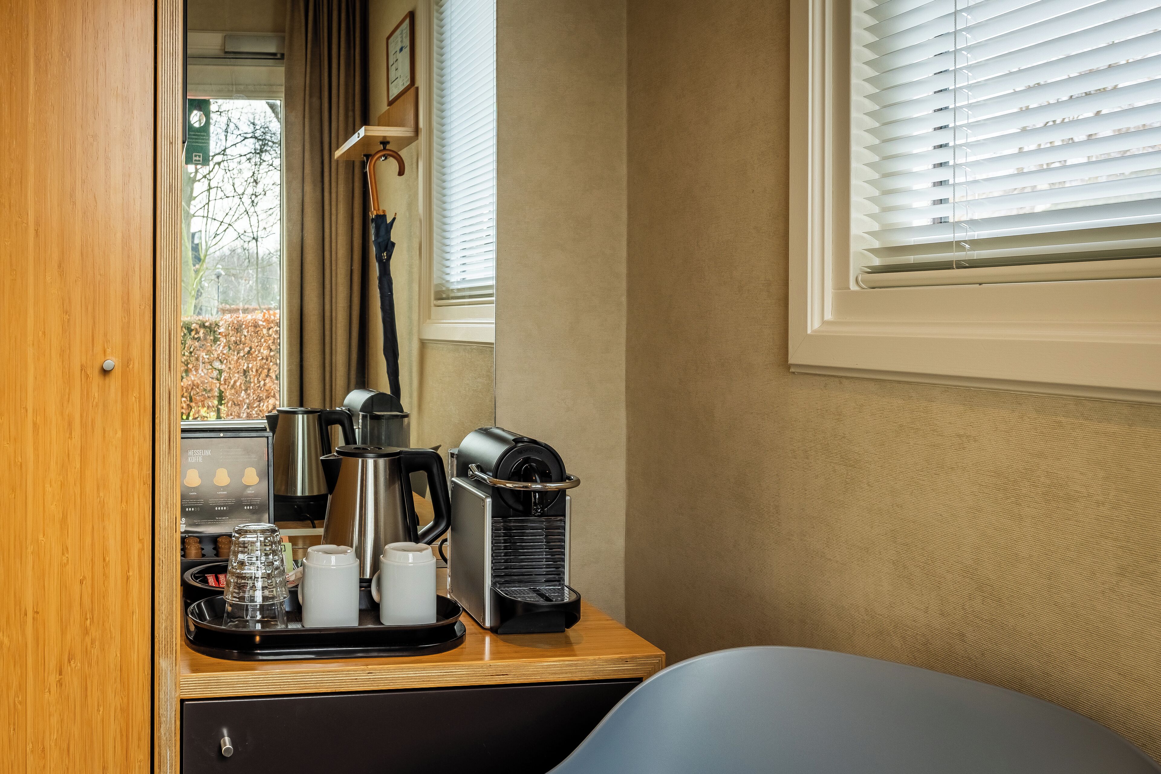 A coffee station with a coffee maker, cups, and a tray.