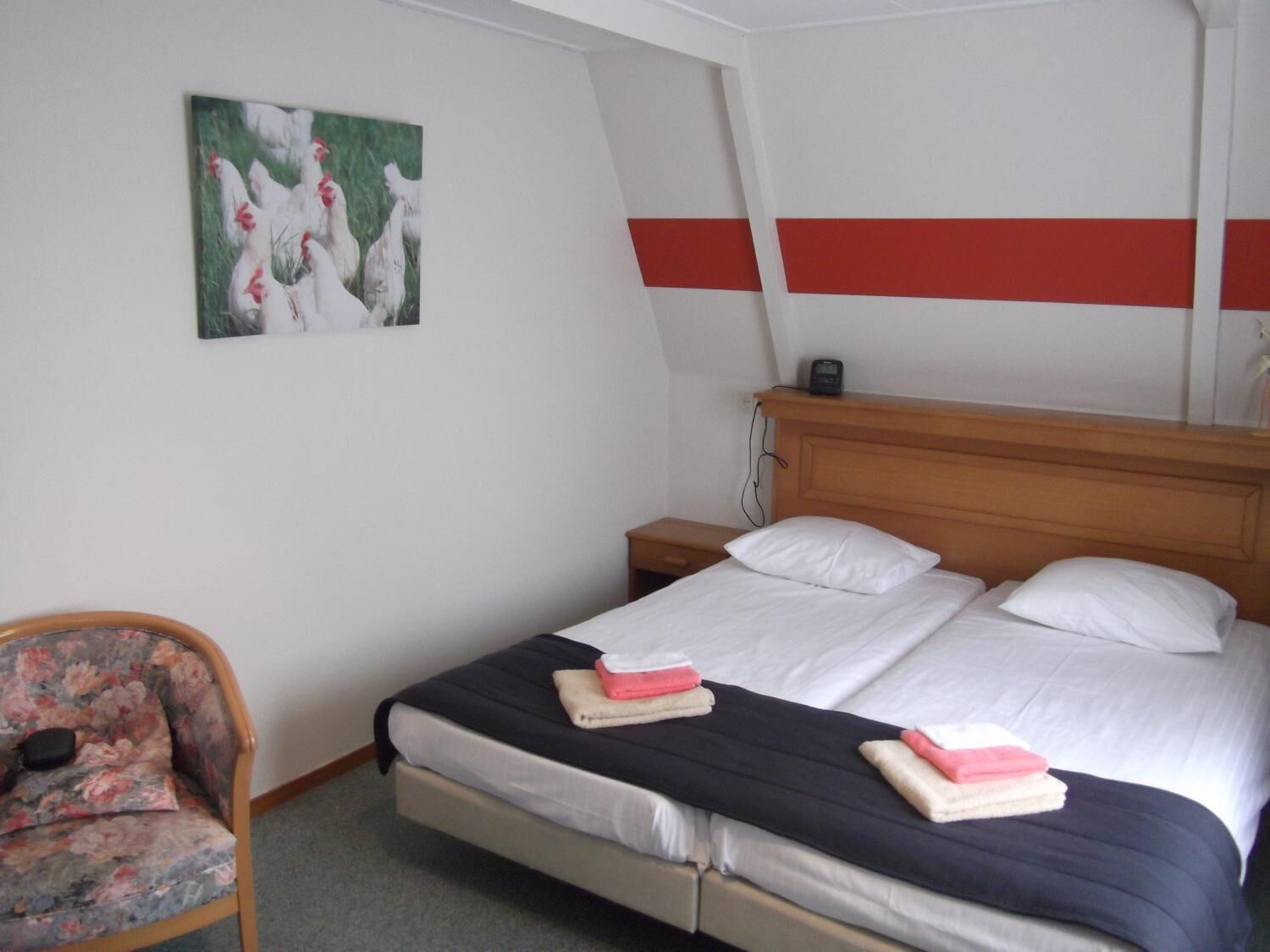 Une chambre d’hôtel avec un lit, une chaise, une table de chevet et un tableau au mur.
