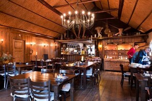 A rustic dining area with wooden tables and chairs, a bar area with shelves of bottles, and a chandelier hanging from the ceiling. - Hotel Boschlust (Oudemirdum)