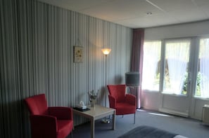 A room with striped wallpaper, two red chairs, a small table with a lamp, a TV on a stand, and a window with curtains. - Hotel Boschlust (Oudemirdum)