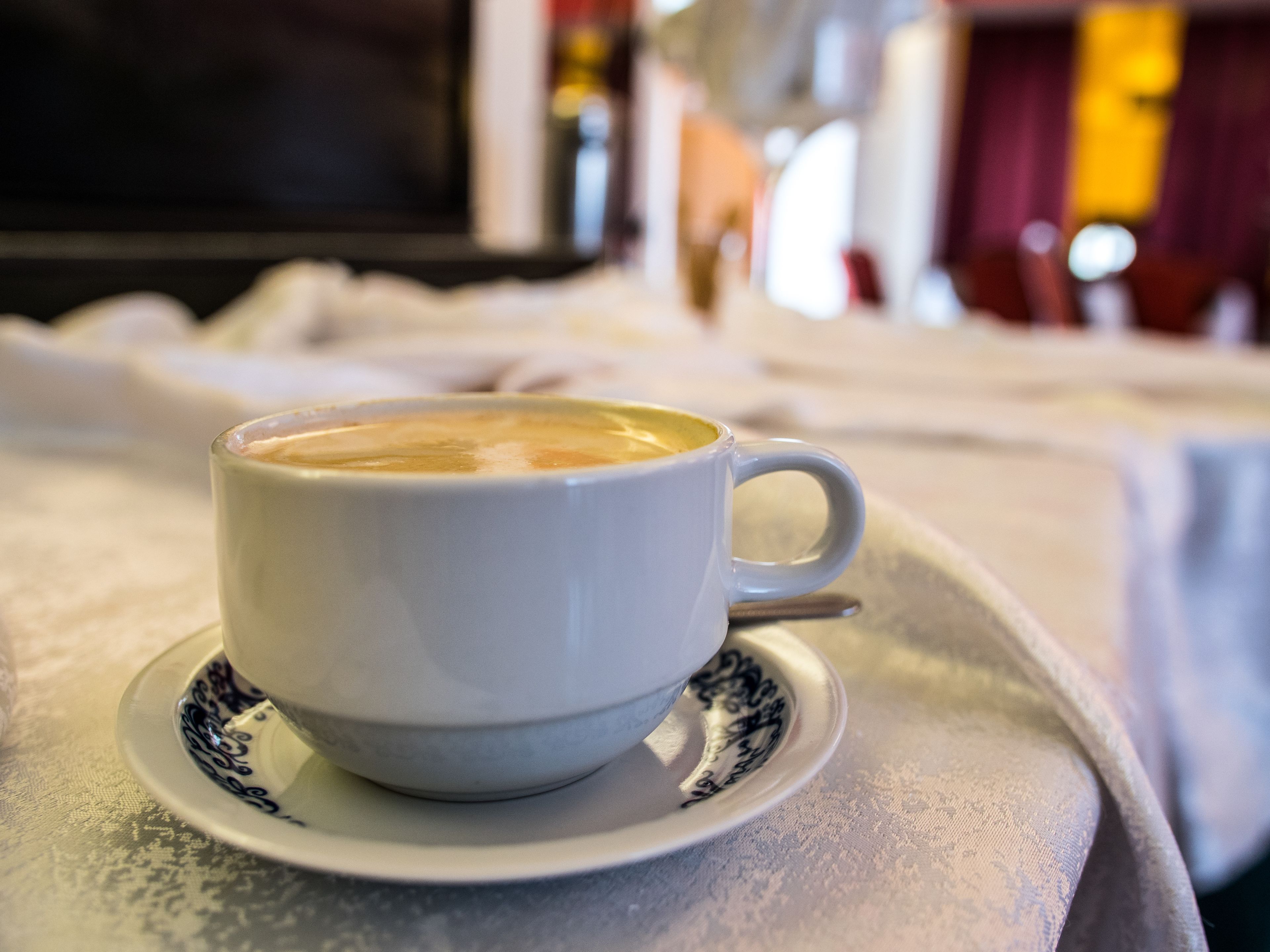 Una taza de café blanco sobre un plato con un borde decorativo, colocada en una bandeja.