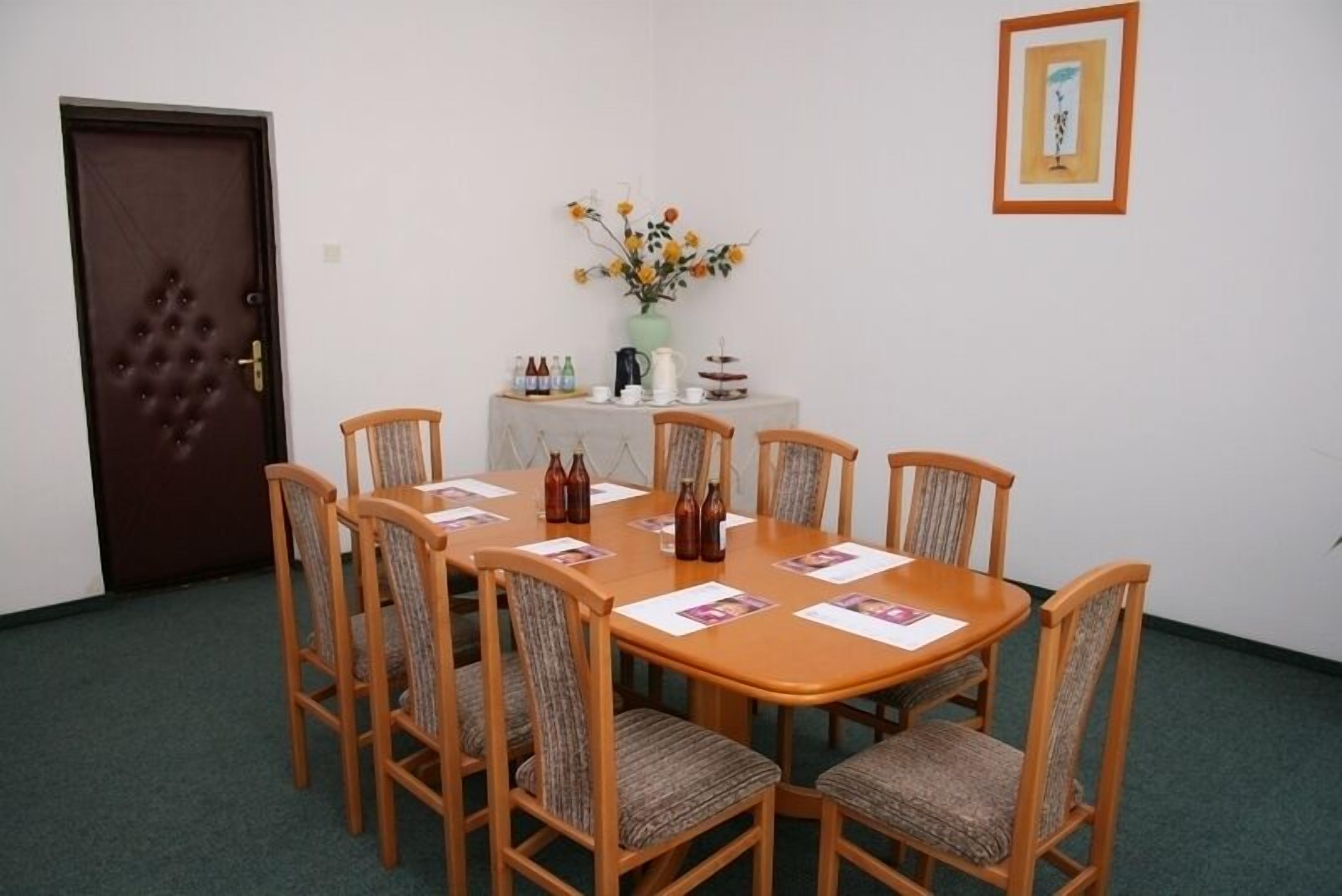 Una sala de conferencias con una mesa redonda, seis sillas, una mesita auxiliar con un jarrón de flores y un cuadro en la pared.