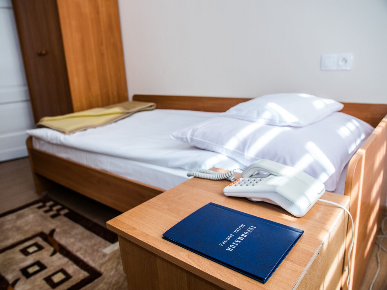 Una habitación de hotel con una cama de madera, ropa de cama blanca, una mesita de noche con un libro y un teléfono.