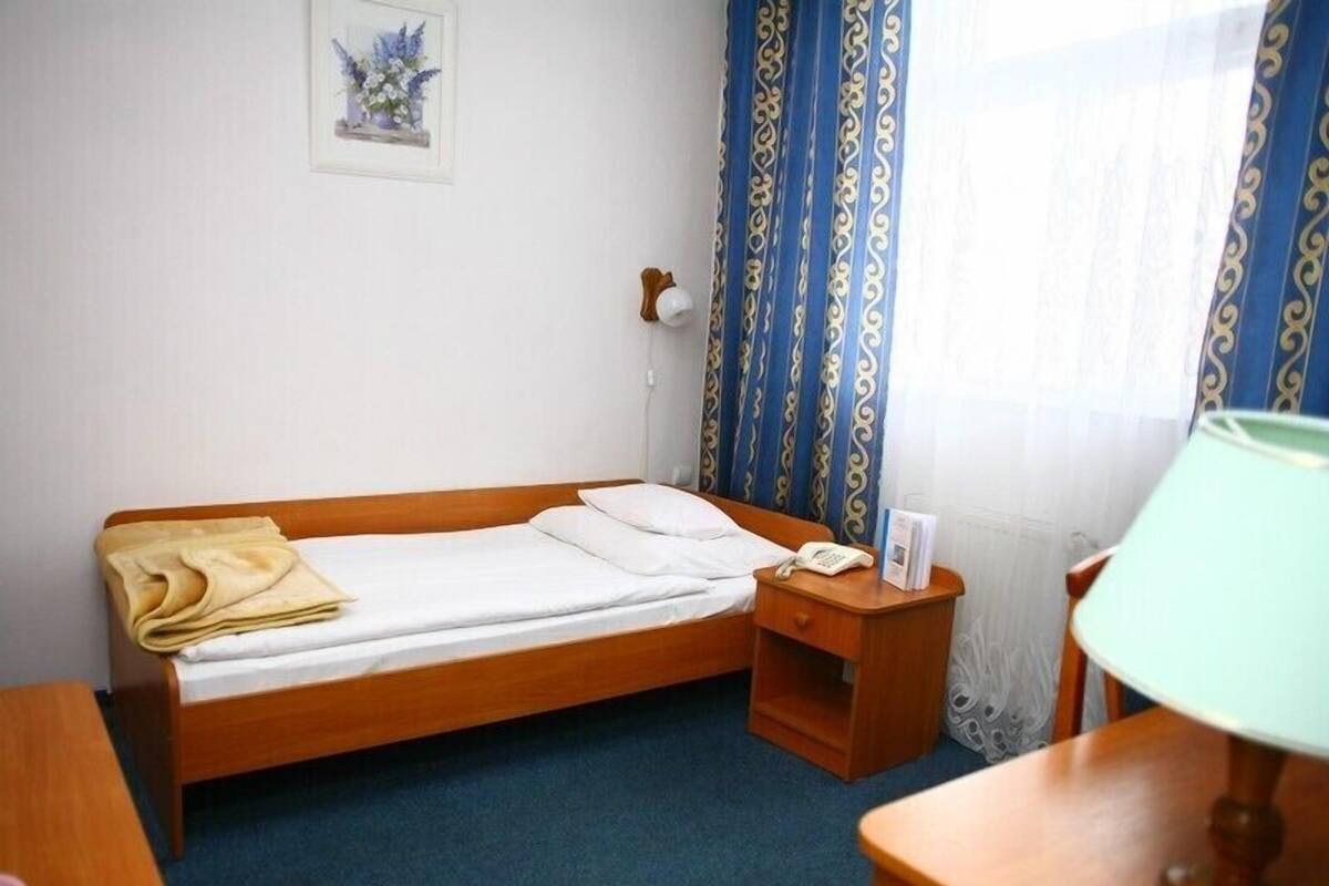 Uma cama de casal com estrutura de madeira, uma mesa de cabeceira com abajur e outra mesa de cabeceira com telefone.