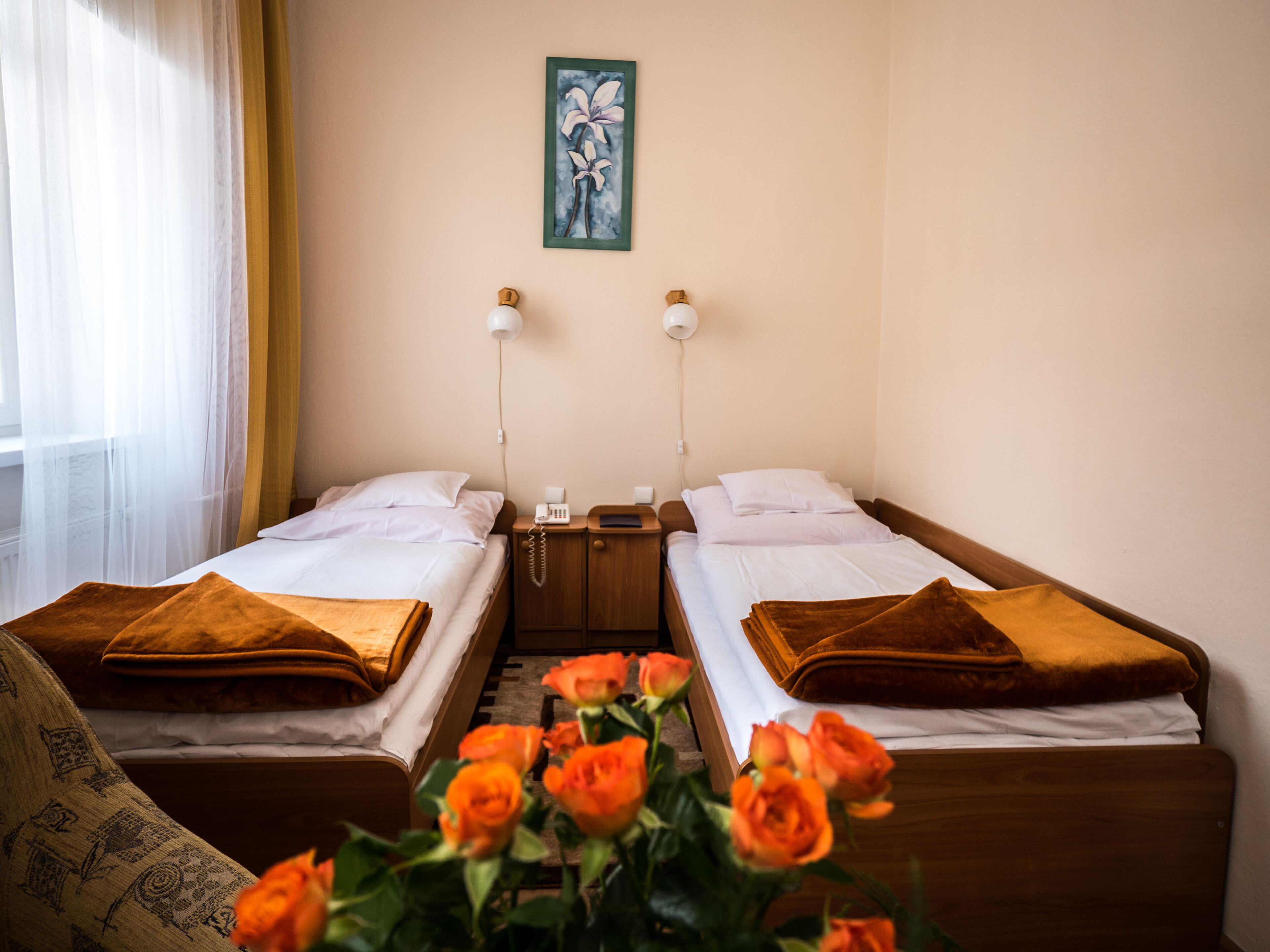 Una habitación de hotel con dos camas individuales, una mesita de noche con lámpara, teléfono y un cuadro en la pared.