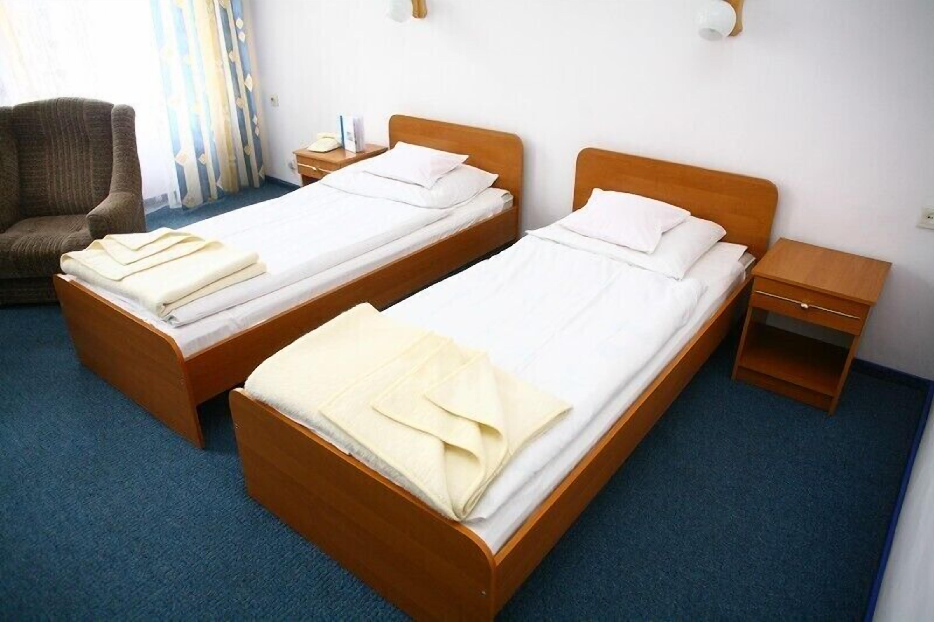 A hotel room with two wooden beds, a chair, a nightstand, and a small wooden table.