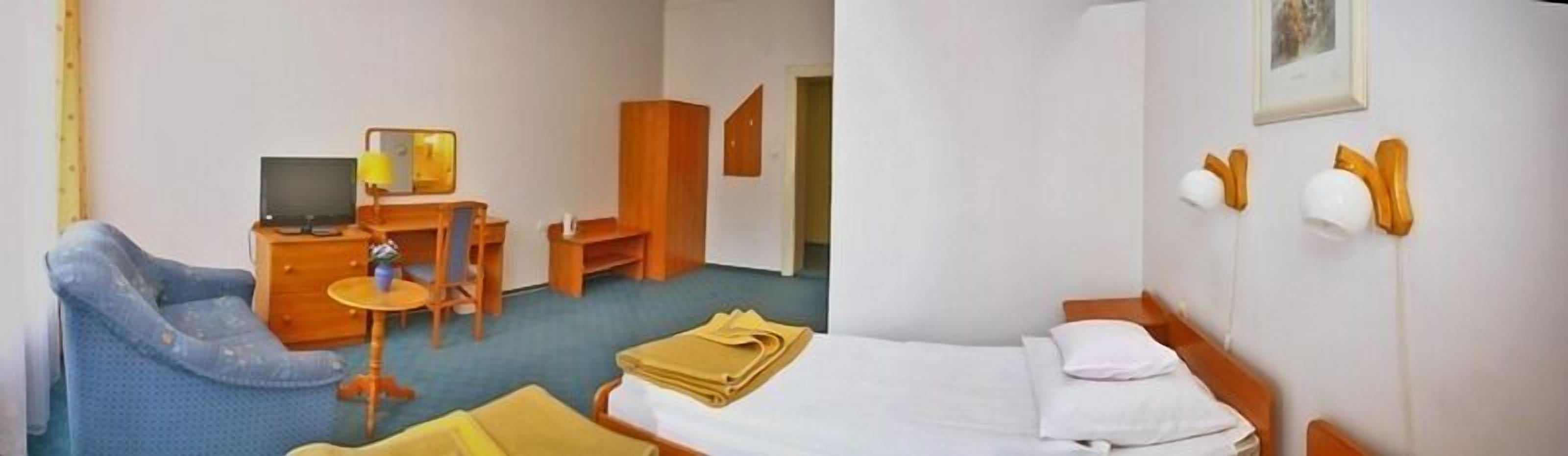 A hotel room with a bed, a desk with a chair, a small table, a TV, and a window.