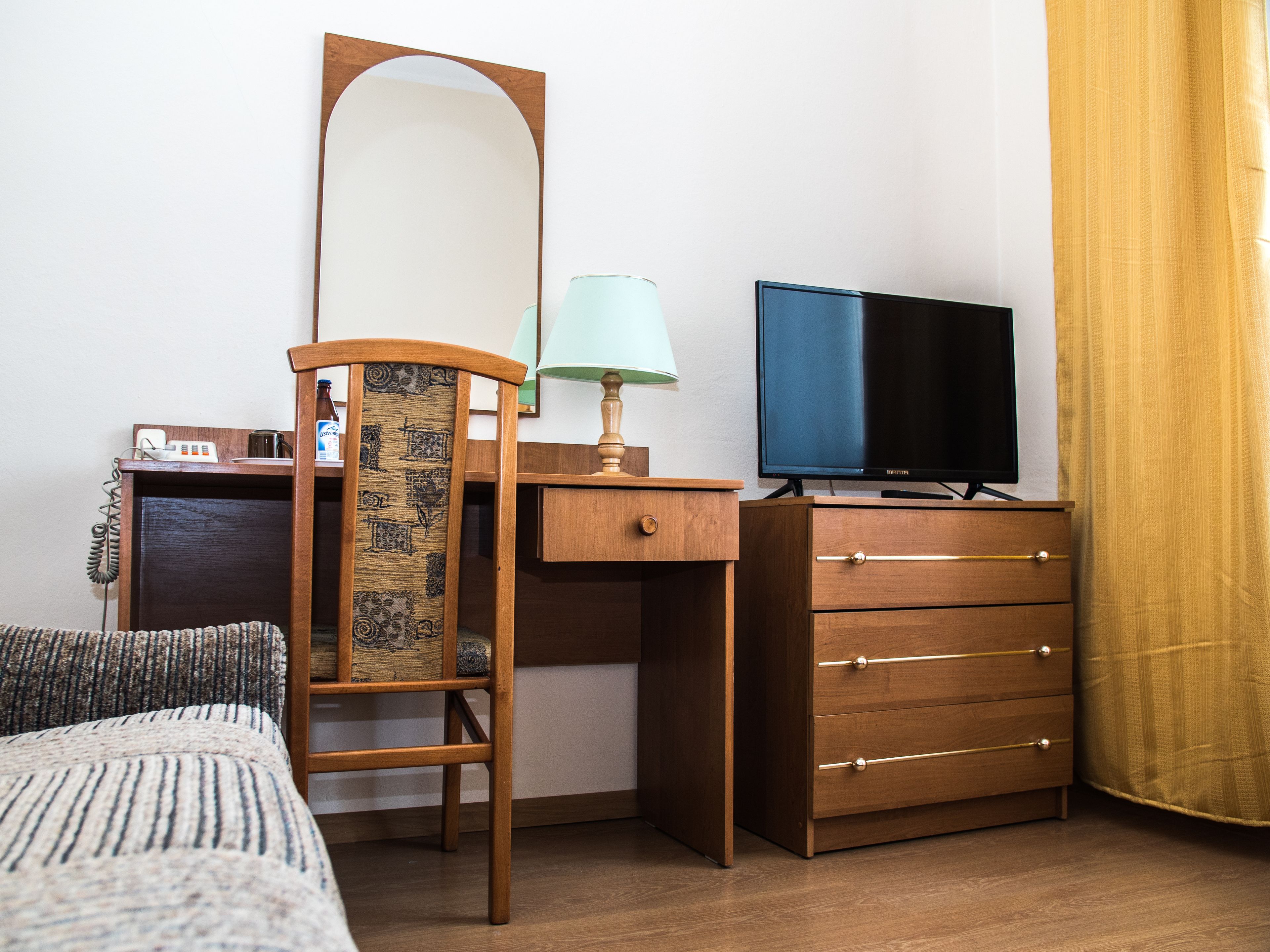 Habitación de hotel con un escritorio de madera, televisor, lámpara, teléfono y cama con ropa de cama a rayas.
