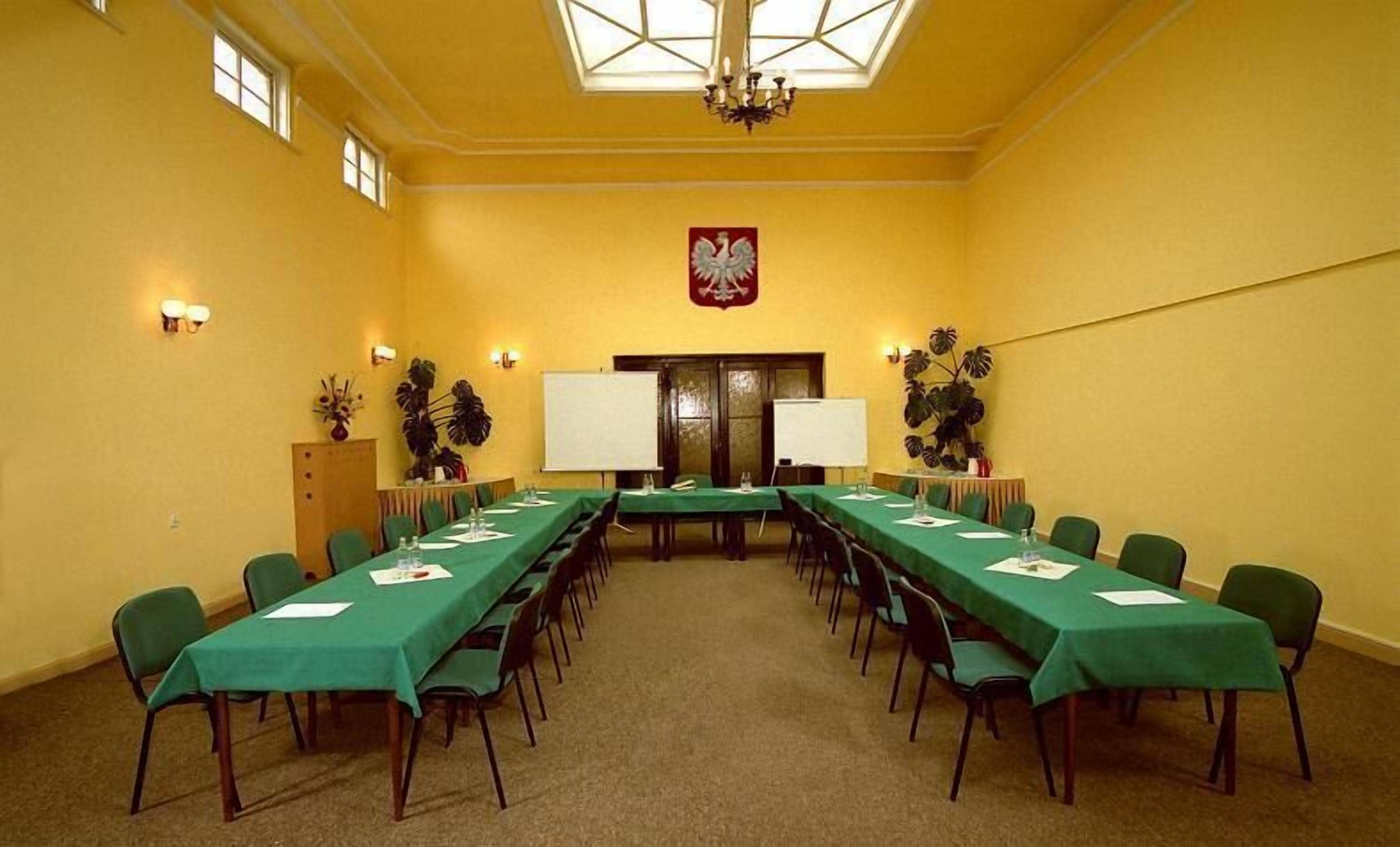 Una sala de conferencias con una larga mesa, sillas, una pizarra y un escudo en la pared.